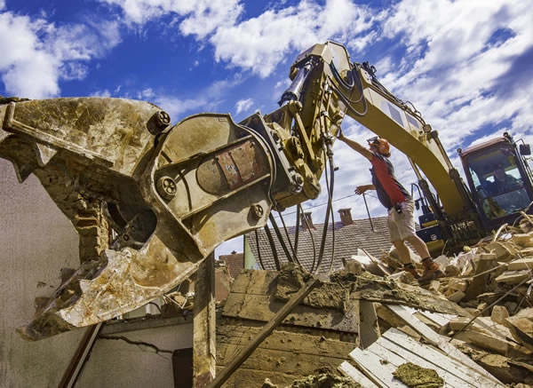 Man examining excavator arm during house demolition